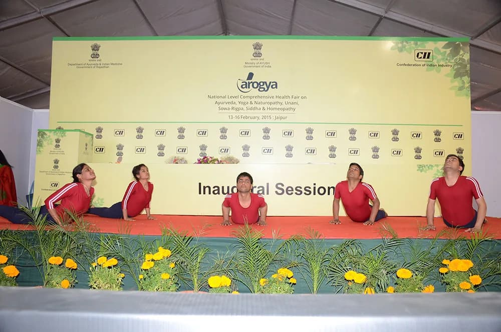 Yoga demonstration on stage during an inaugural session, with marigold borders