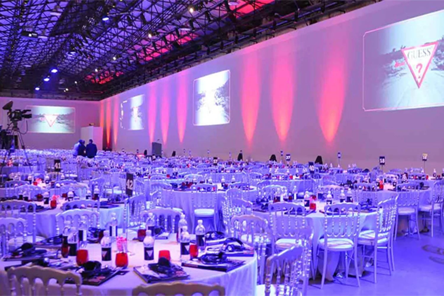 Large hall lit in violet and pink with banquet tables and projection screens